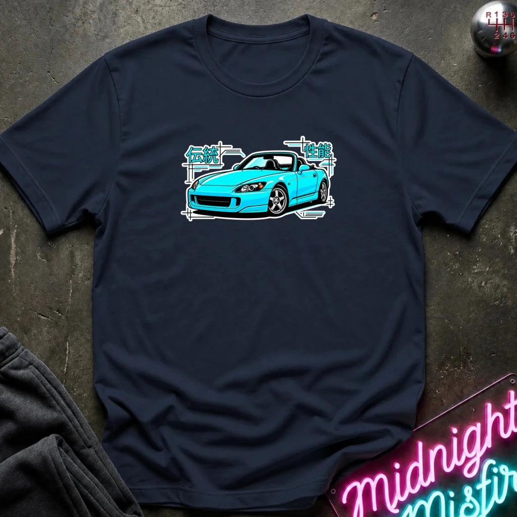 navy t-shirt laid flat on a dark textured surface, featuring a graphic print of a bright blue sports car with white and teal text elements. A neon sign and dark clothing are partially visible in the styled flat-lay composition.