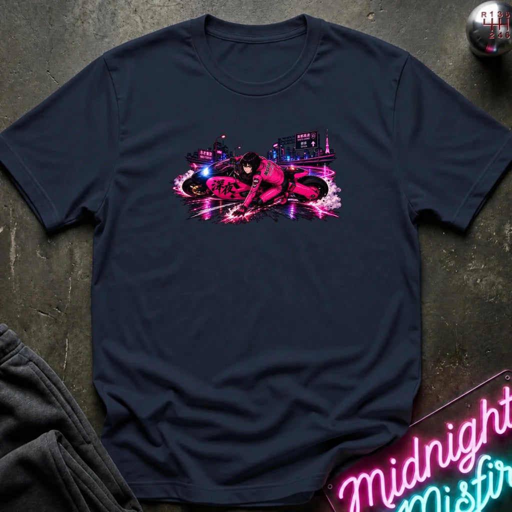 A navy blue crewneck t-shirt laid flat on a dark textured surface, featuring a vibrant neon graphic of a motorcycle racer on the chest. The shirt is styled with dark gray sweatpants, a neon sign, and a small metallic object in the corners.