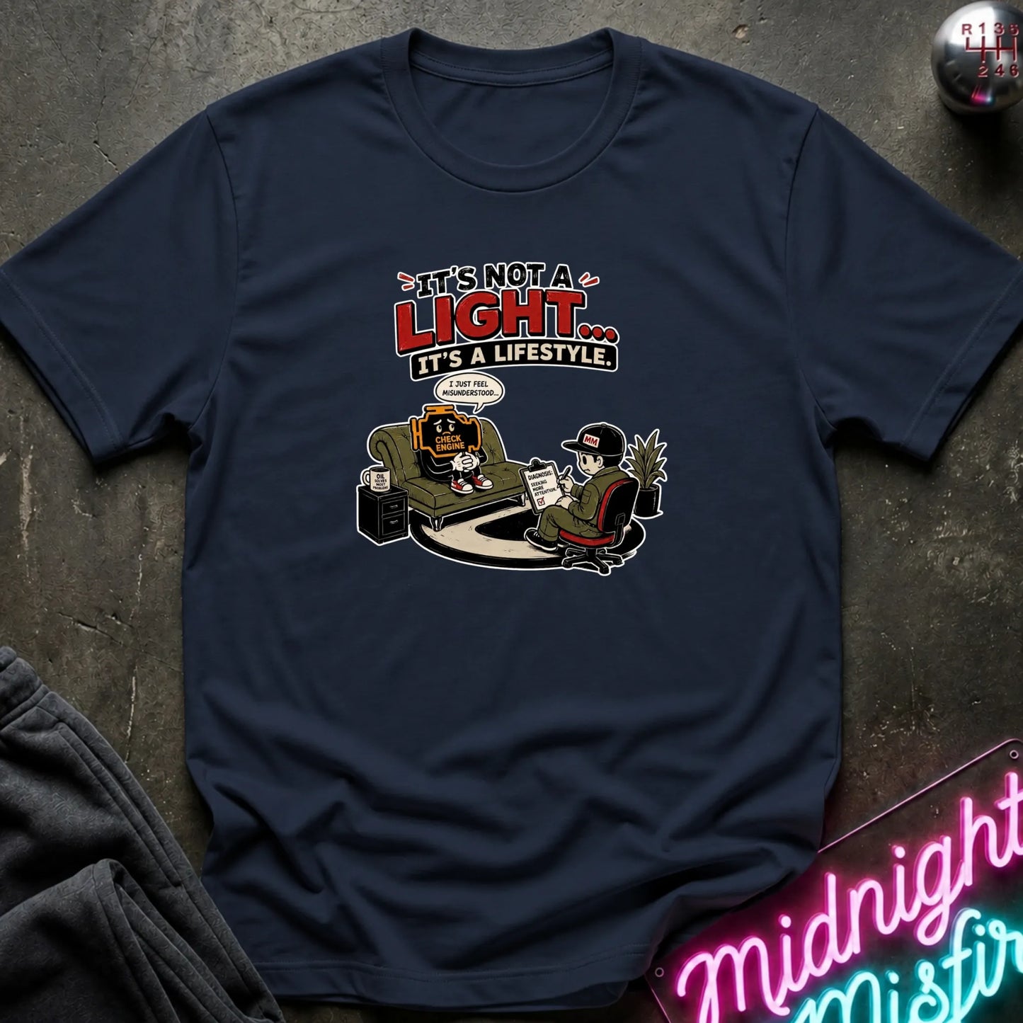 A navy blue graphic t-shirt laid flat on a dark textured surface. The shirt features a cartoon with the text 'IT'S NOT A LIGHT.