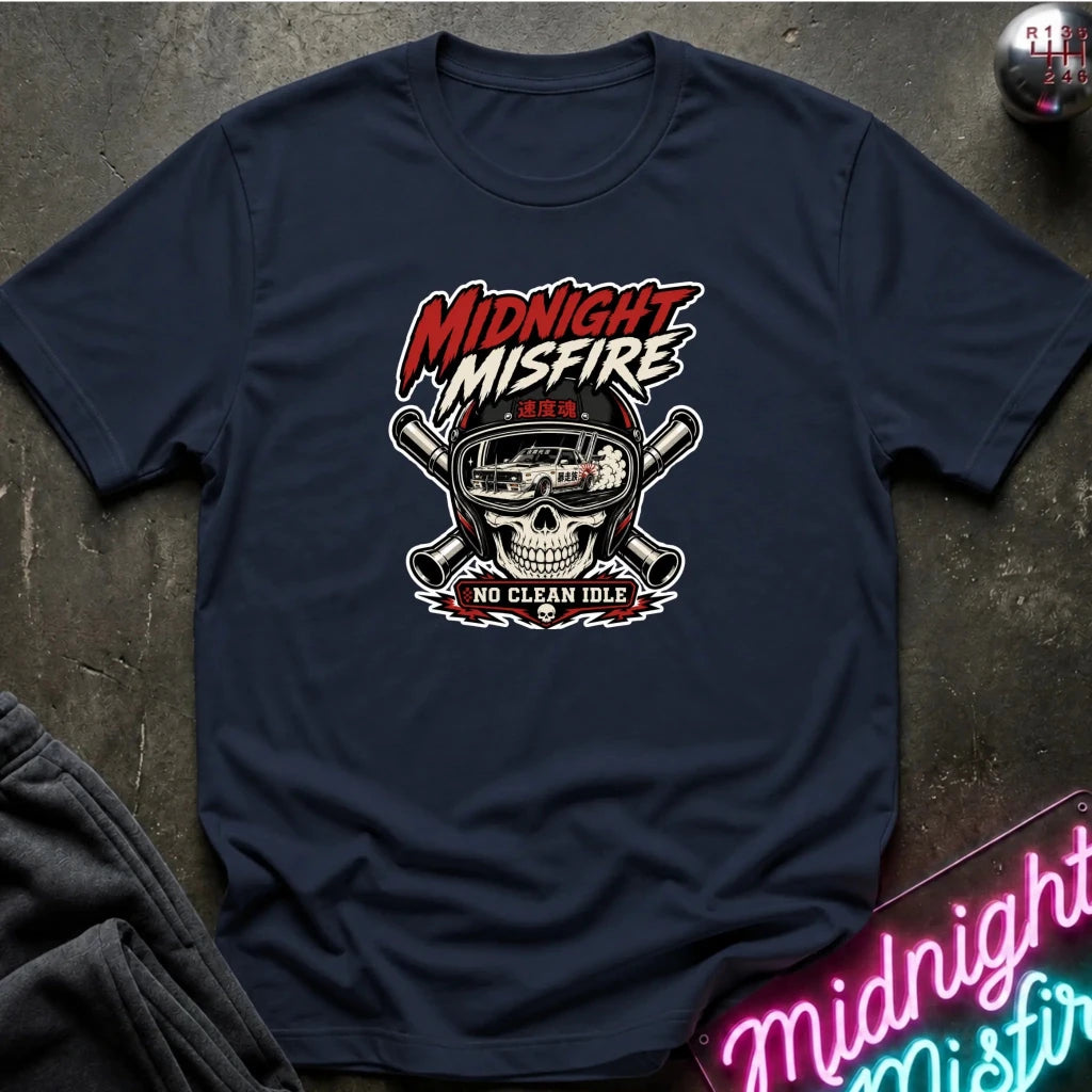 A navy blue graphic t-shirt laid flat on a dark textured surface. The shirt features a central graphic of a skull wearing a racing helmet with crossed pipes behind it, and the text 'MIDNIGHT MISFIRE' and 'NO CLEAN IDLE'.