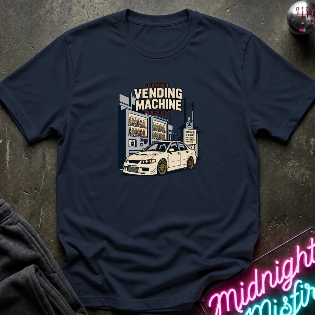 A navy blue crewneck t-shirt laid flat on a dark textured surface, featuring a retro-style graphic of a white sports car parked in front of a vending machine with the text 'VENDING MACHINE'.