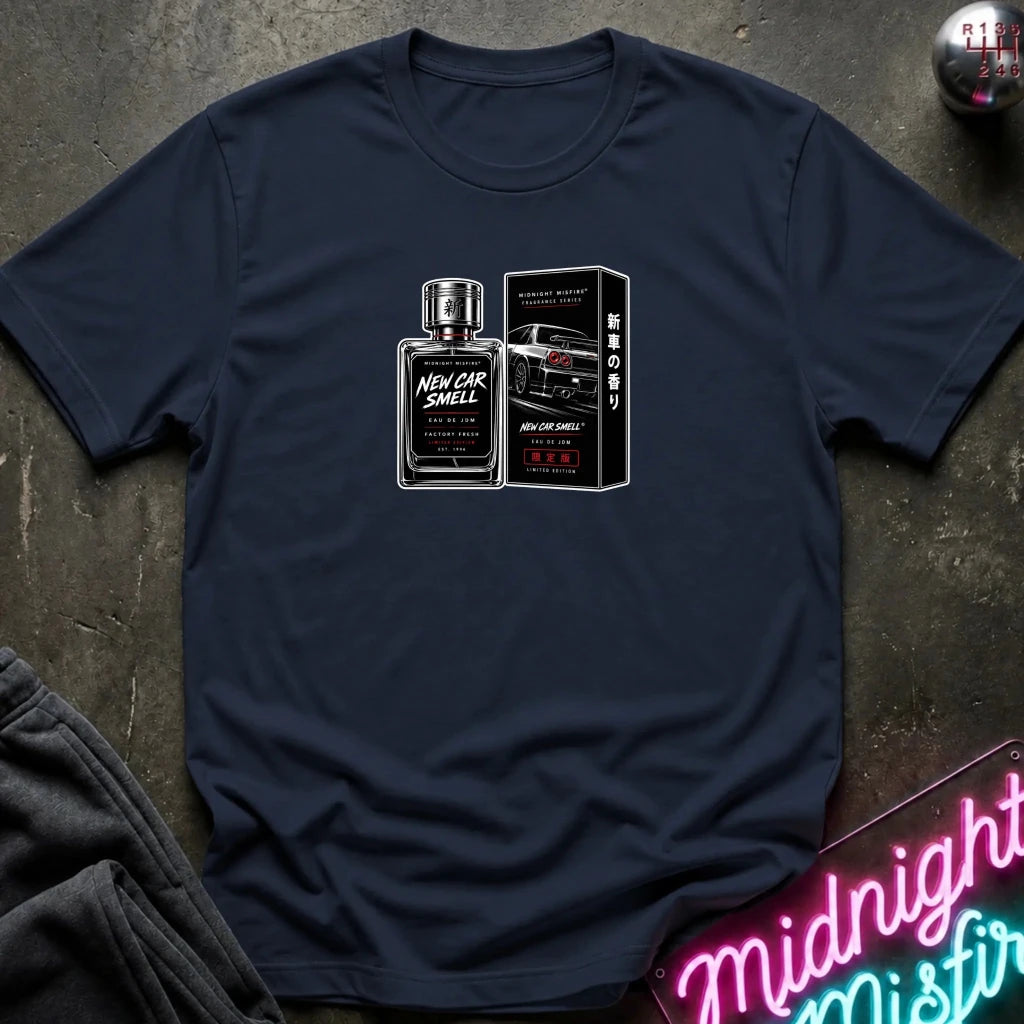 A navy blue crewneck t-shirt laid flat on a dark textured surface, featuring a graphic print of a 'New Car Smell' perfume bottle and box with a sports car. 