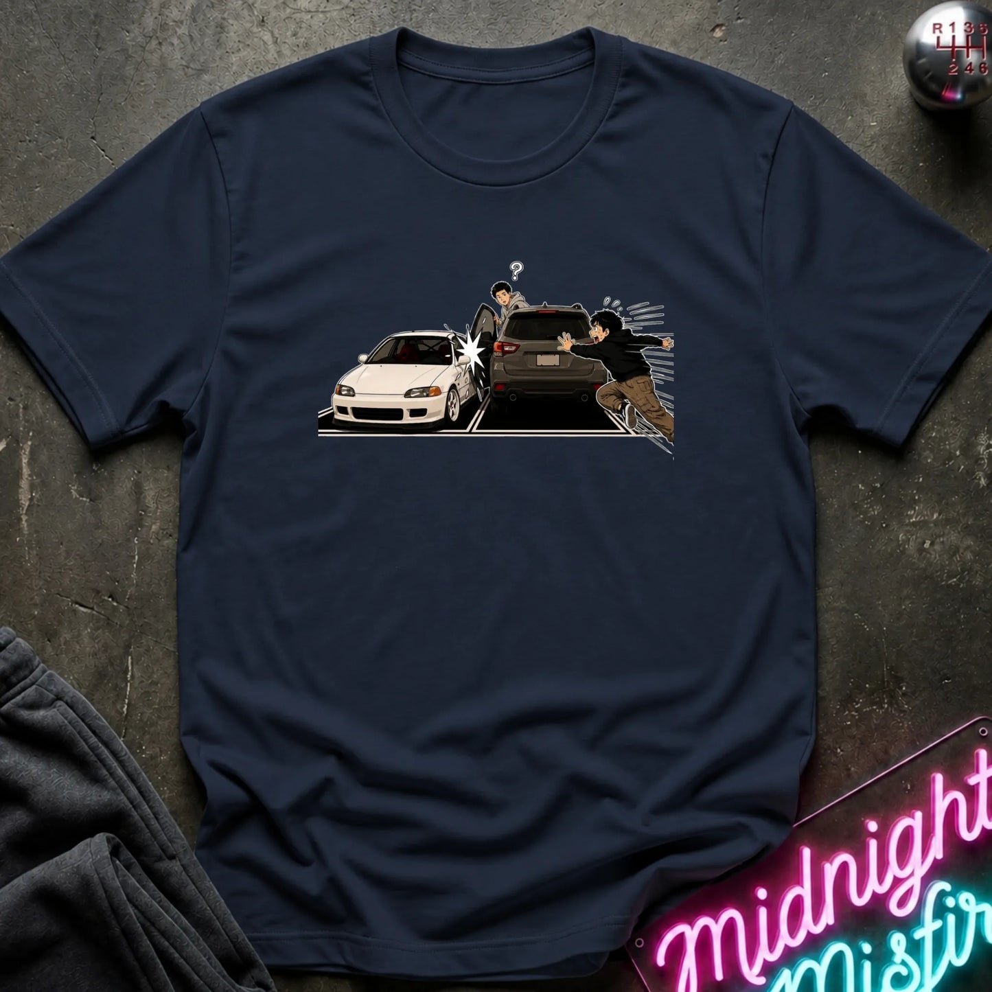 A navy blue short-sleeve t-shirt laid flat on a dark textured surface, featuring a graphic print of a white sports car and a black SUV with two figures in a street scene. 