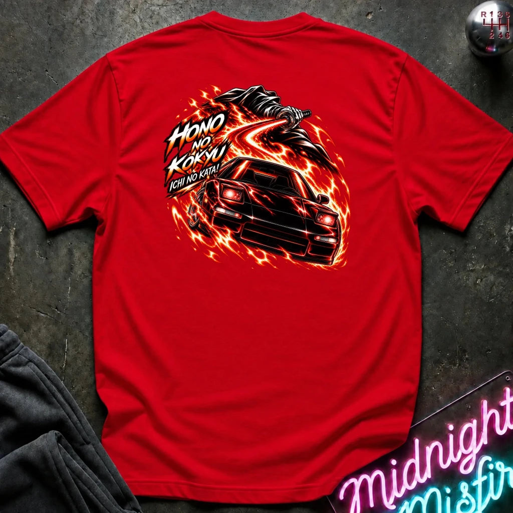 A red short-sleeve t-shirt laid flat on a dark textured surface, showing the back graphic with a car and the text "ichi no kata!"