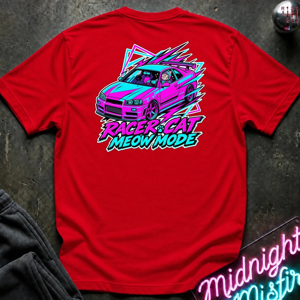 A bright red short-sleeve t-shirt laid flat on a dark textured surface, featuring a colorful graphic of a pink and teal race car with the text 'RACER CAT MEOW MODE' in neon-style lettering.