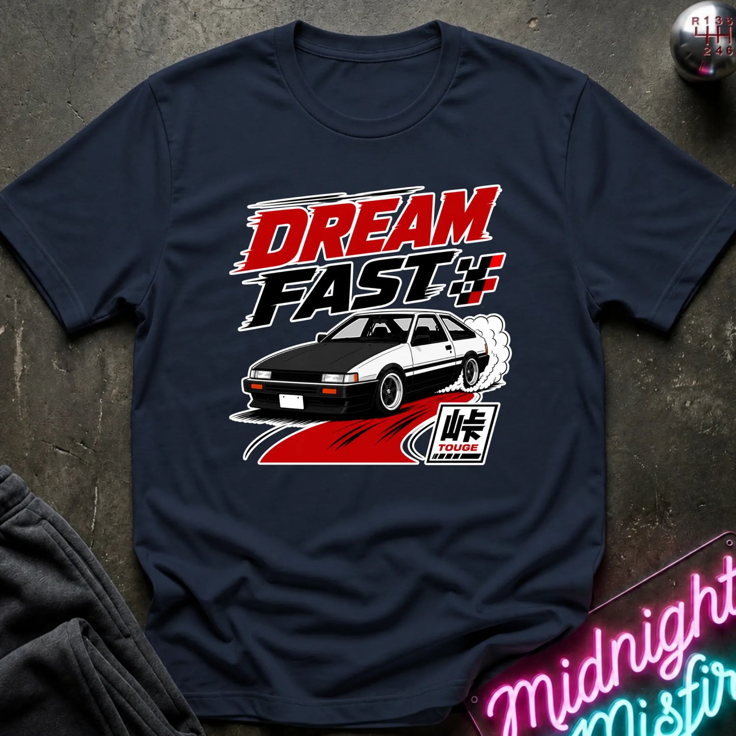 A navy blue graphic t-shirt featuring the 'Dream Fast 4' design with a white and black sports car, red and white text, and a 'Takotchimes' logo, laid flat on a dark textured surface.