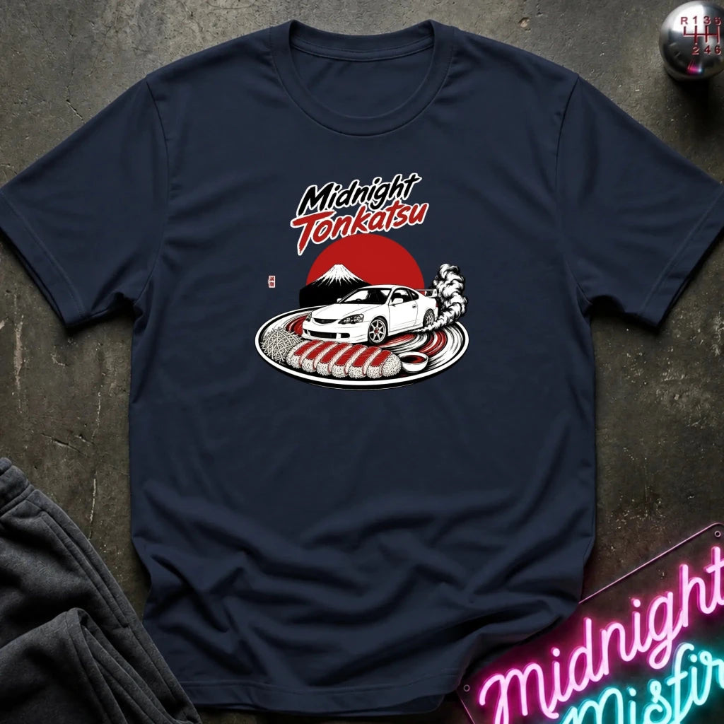 A navy blue graphic t-shirt laid flat on a dark textured surface. The shirt features a circular graphic in the center with the text 'Midnight Tenkatsu' in red and white, above an illustration of a white sports car, a samurai, and a red sun over Mount Fuji.