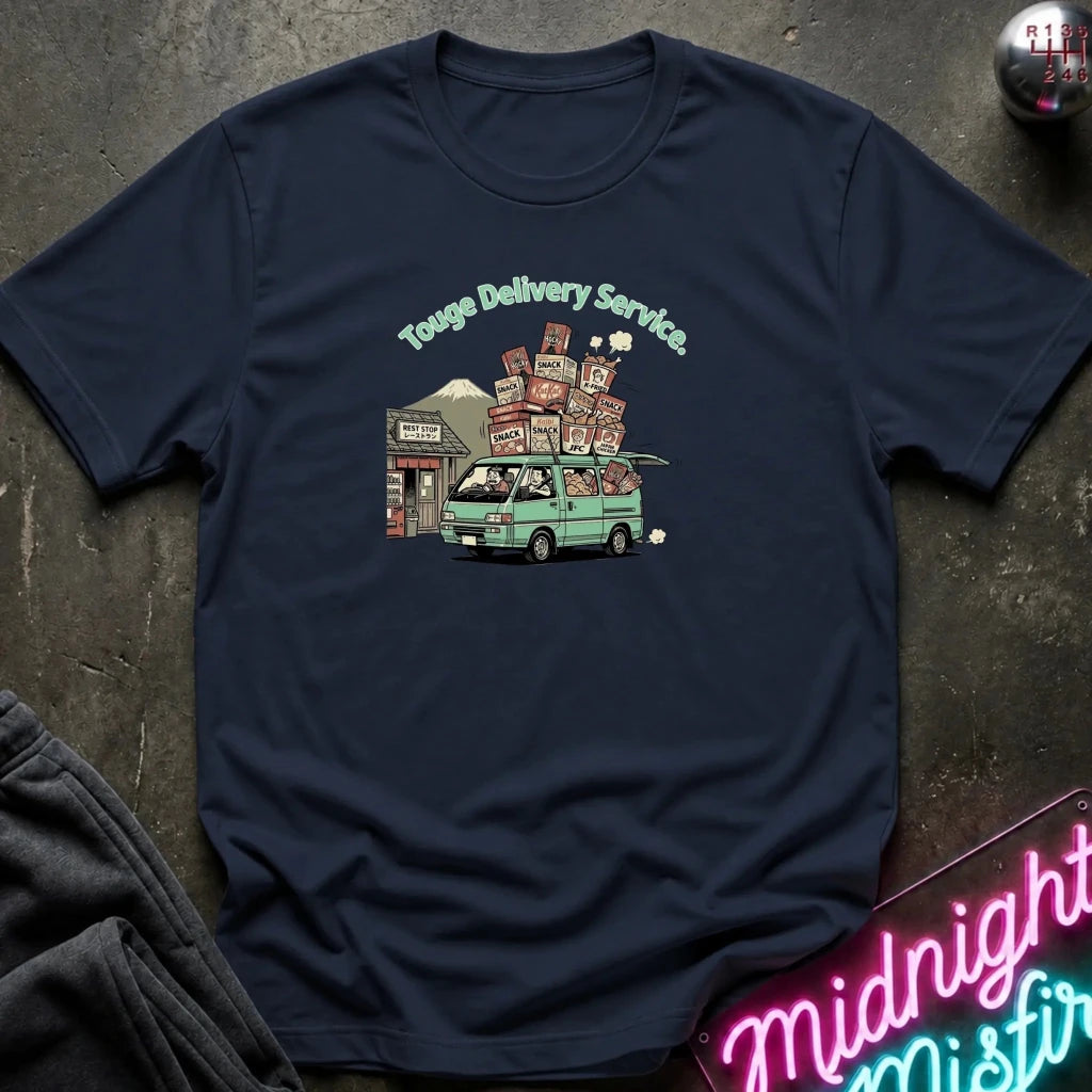 A navy blue short-sleeve t-shirt laid flat on a dark textured surface, featuring a colorful graphic of a green van carrying stacked boxes with the text 'Touge Delivery Service.' printed above it.