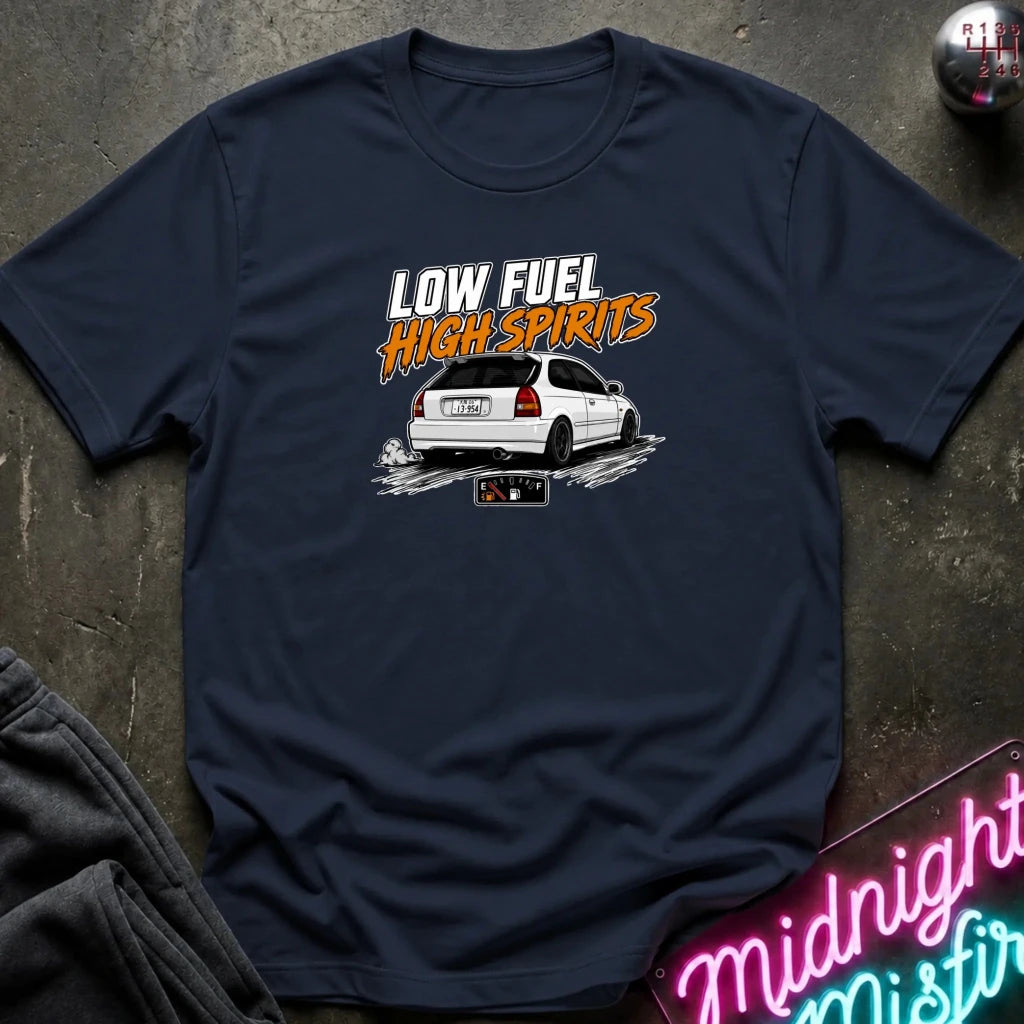 A navy blue graphic t-shirt laid flat on a dark textured surface. The graphic features the text 'LOW FUEL HIGH SPIRITS' in white and orange above a white station wagon with a license plate reading 'LOW FUEL'.