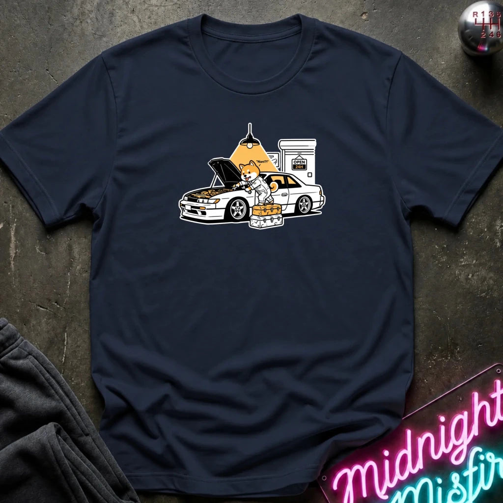 navy graphic t-shirt laid flat on a dark textured surface. The graphic features a dog fixing a car.