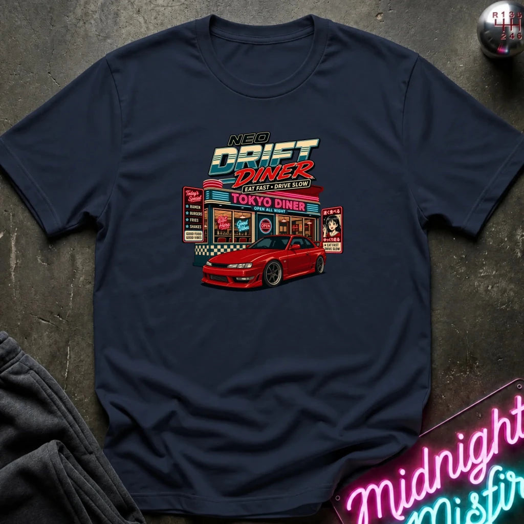 A navy blue t-shirt laid flat on a dark textured surface, featuring a colorful graphic print of a red sports car parked outside a retro 'Neon Drift Diner' with neon sign props in the corner.
