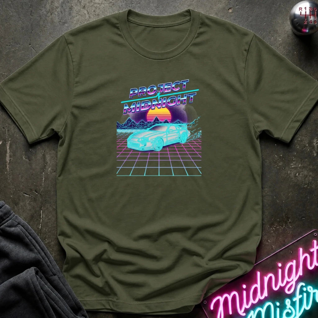 An olive green short-sleeve t-shirt with a retro 80s synthwave graphic reading 'PROTECT MIDNIGHT' above a neon car and grid scene, laid flat on a dark textured surface with partial jeans and a neon sign visible around it.