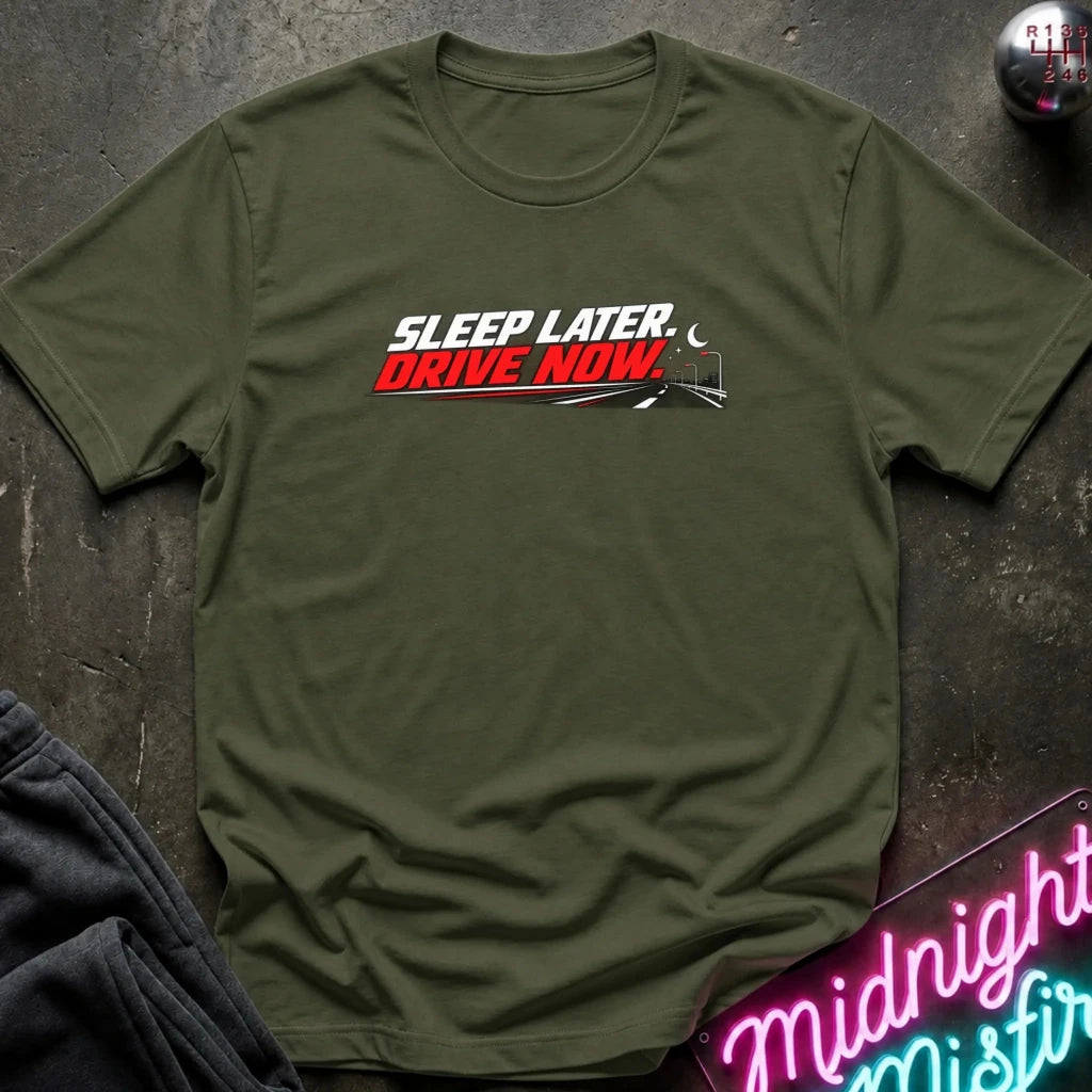 An olive green short-sleeve t-shirt with a graphic print reading 'SLEEP LATER. DRIVE NOW.