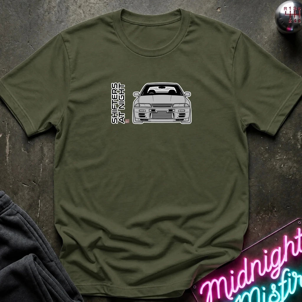 An olive green short-sleeve t-shirt laid flat on a dark textured surface, featuring a white graphic of a sports car and the vertical text 