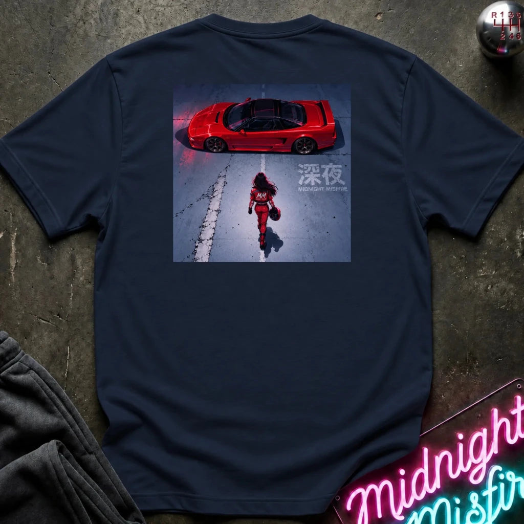 A navy blue short-sleeve t-shirt laid flat on a dark textured surface, featuring a large rectangular graphic print on the back. The graphic shows a red sports car in a snowy scene with a person walking