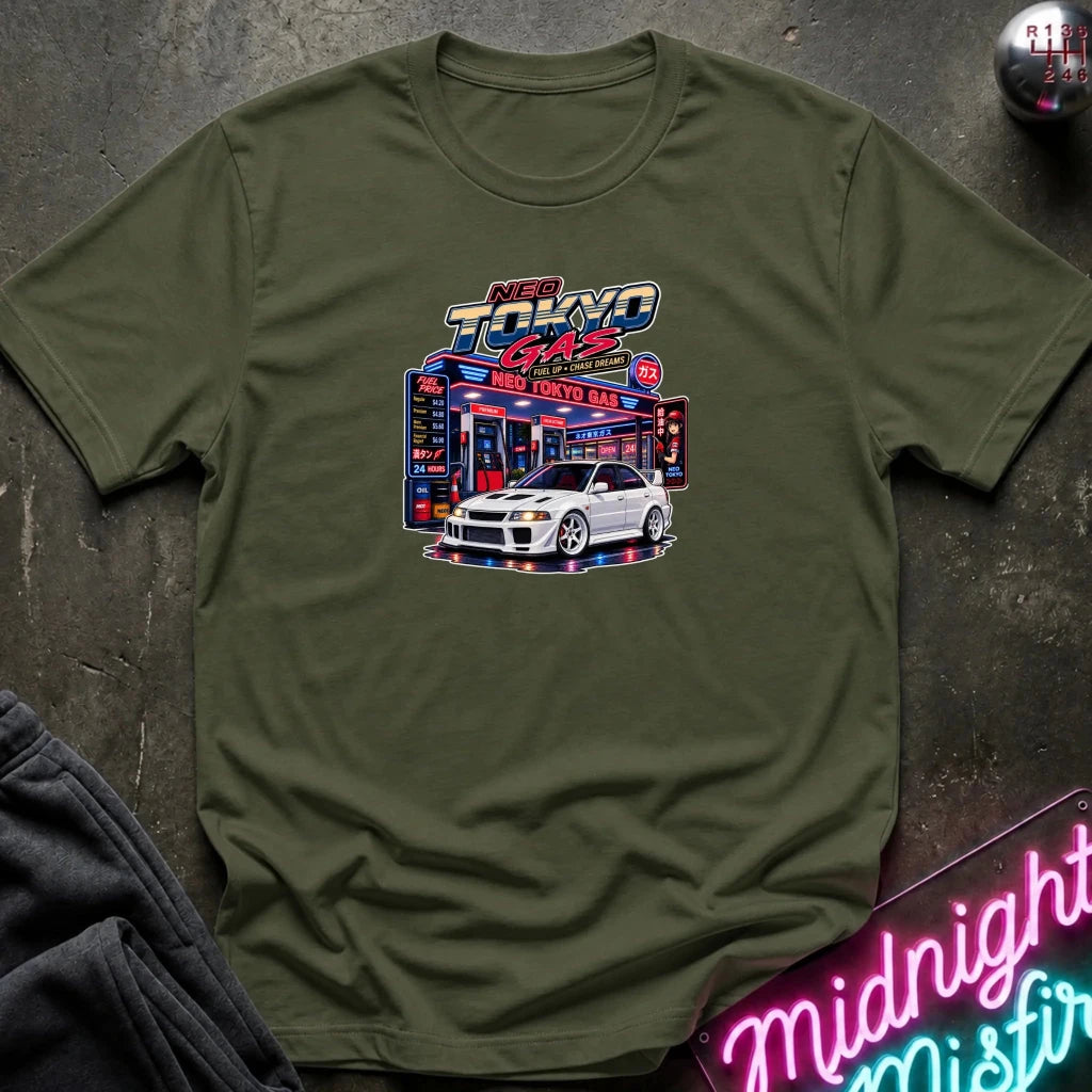 A olive green short-sleeve crewneck t-shirt featuring a 'Neo Tokyo Gas' graphic with a white sports car, laid flat on a dark textured surface with a neon sign and sweatpants as props.
