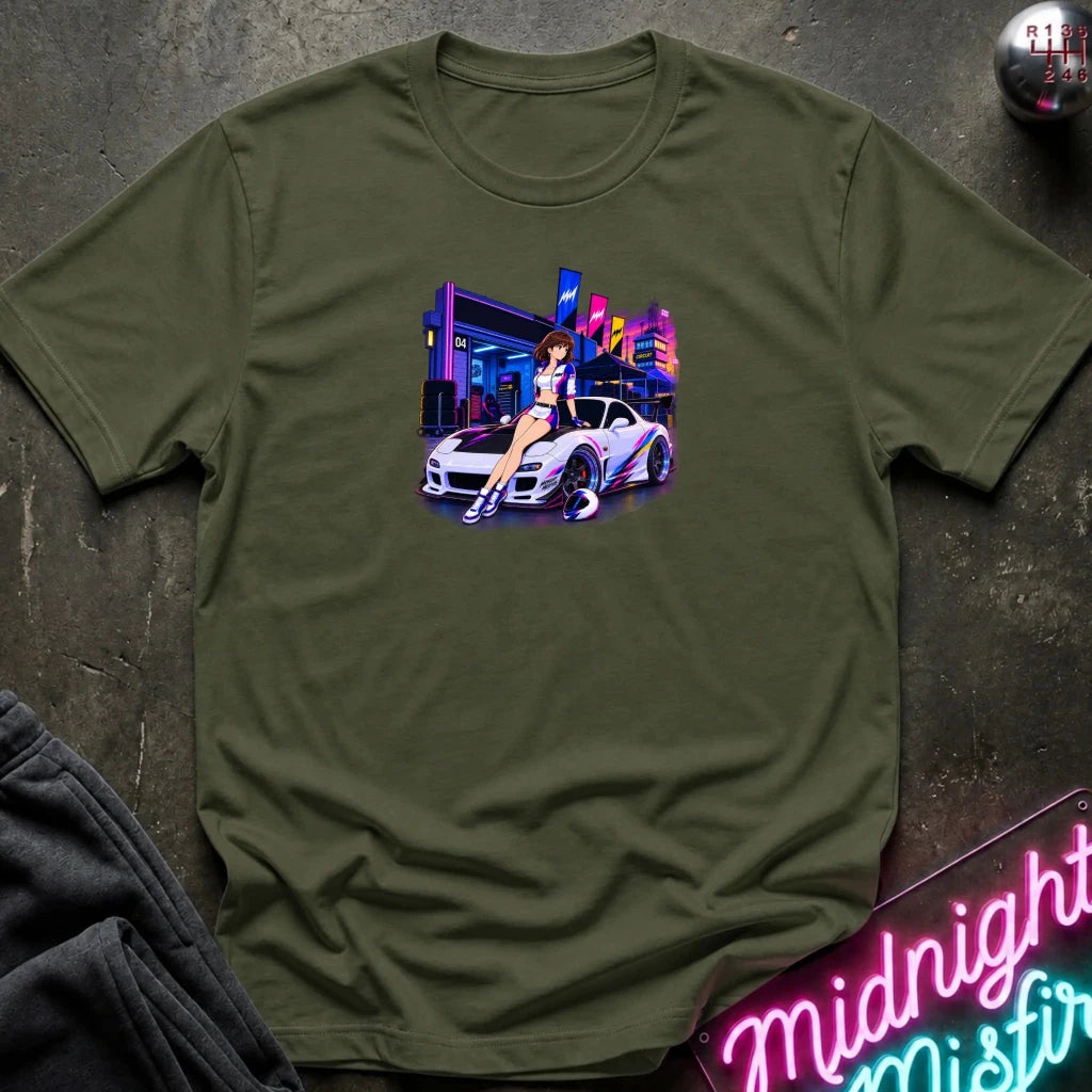 An olive green short-sleeve t-shirt laid flat on a dark textured surface, featuring a colorful graphic print of a white sports car and a woman in a neon-lit scene. 