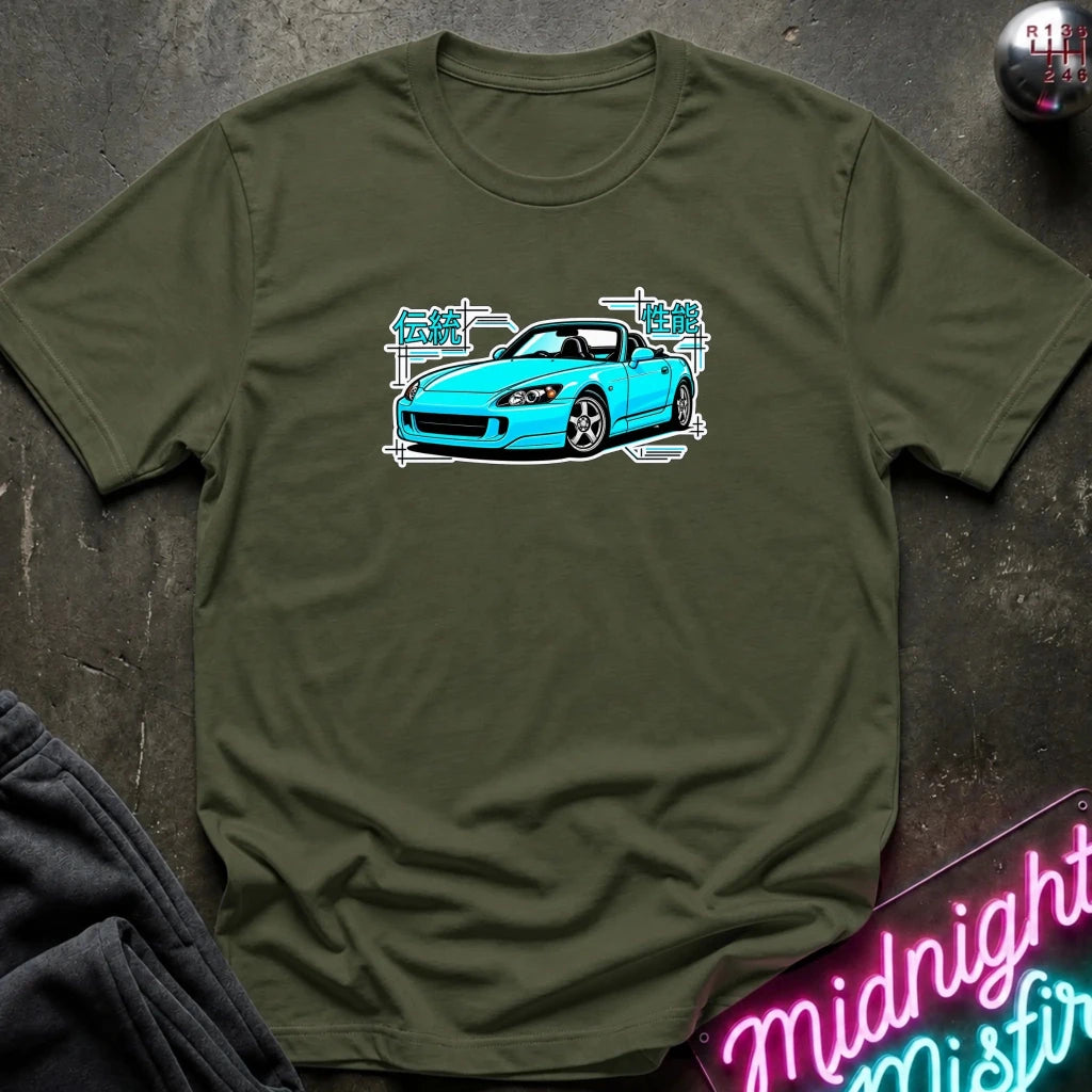 olive green t-shirt laid flat on a dark textured surface, featuring a graphic print of a bright blue sports car with white and teal text elements. A neon sign and dark clothing are partially visible in the styled flat-lay composition.