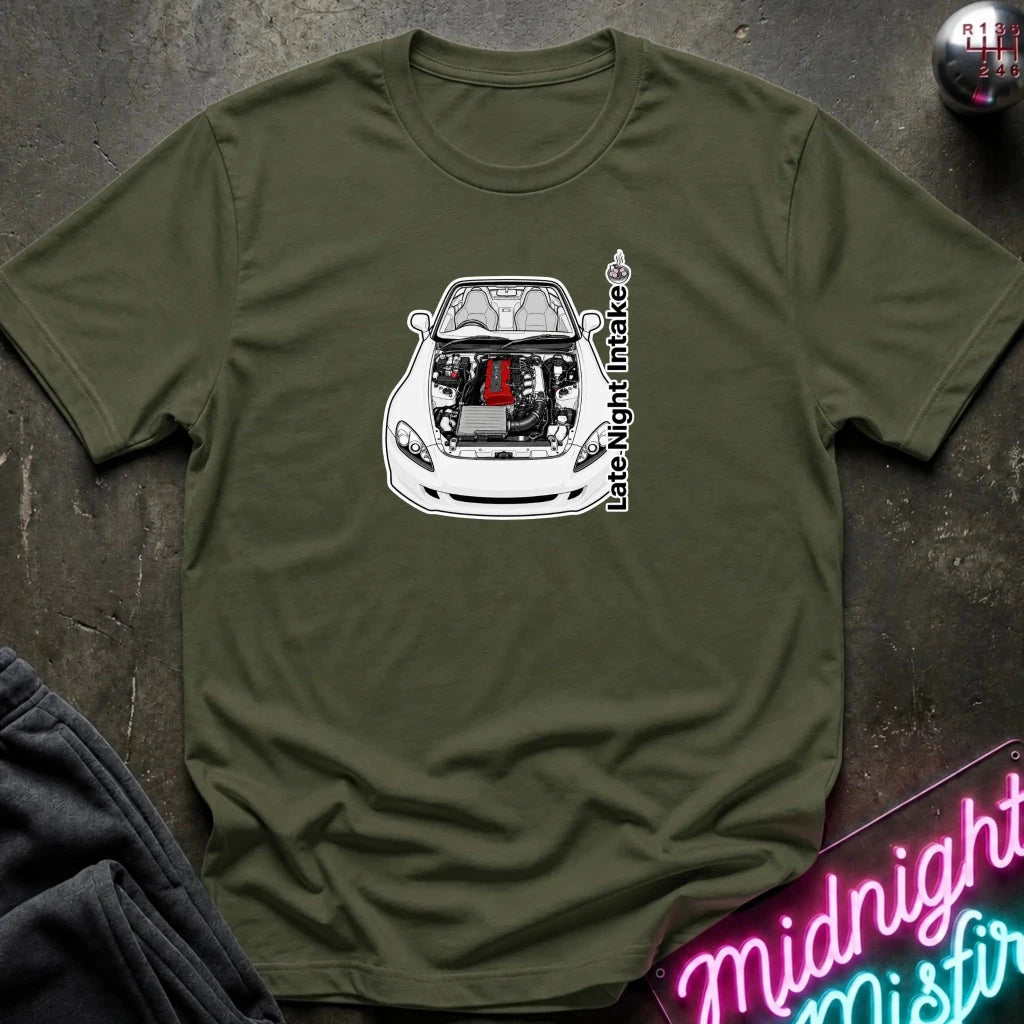 An olive green crewneck t-shirt laid flat on a dark textured surface, featuring a graphic of a white sports car with its hood open, revealing a red engine block. The text 'late night intake' is printed vertically next to the car.