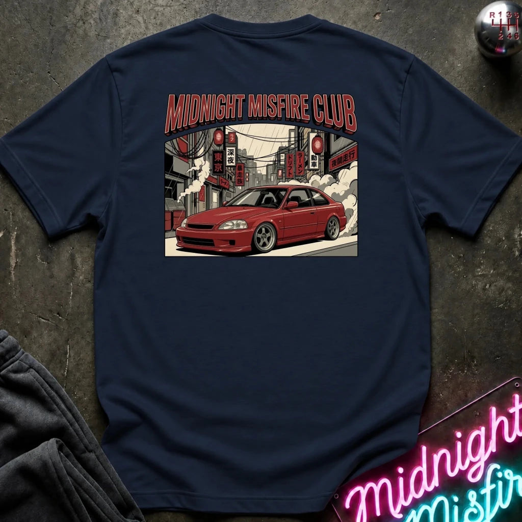 A navy blue t-shirt laid flat on a dark textured surface, featuring a large graphic print on the back with the text 'MIDNIGHT MISFIRE CLUB' above an illustration of a red sports car drifting in a city street. 
