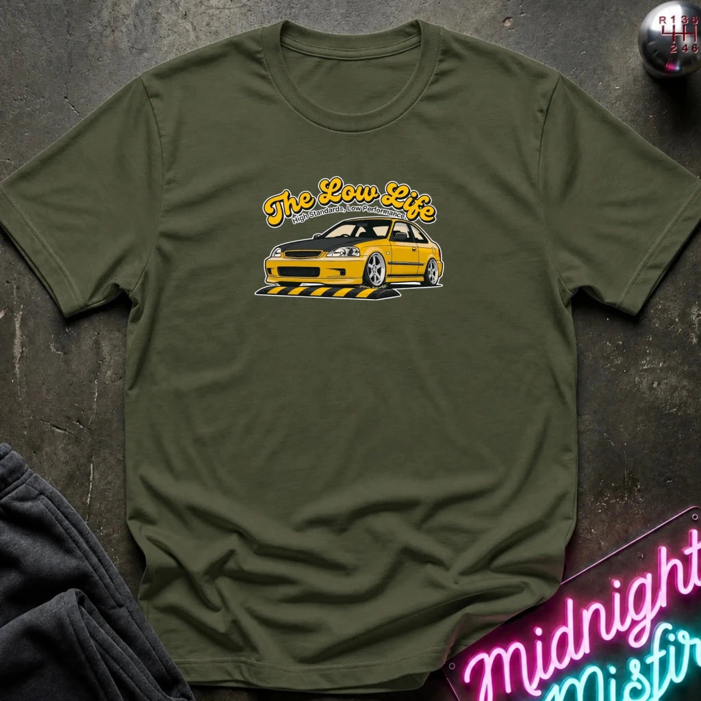 green  t-shirt laid flat on a dark textured surface, featuring a graphic of a yellow sports car with the text 'The Low Life' in yellow script. 