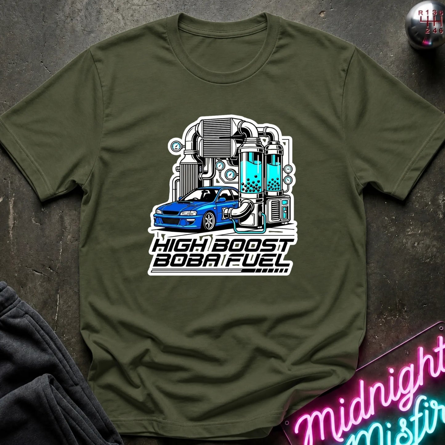 An olive green short-sleeve t-shirt with a 'High Boost Boba Fuel' graphic on the chest, styled flat on a dark textured surface with a neon sign and dark fabric in the corners.