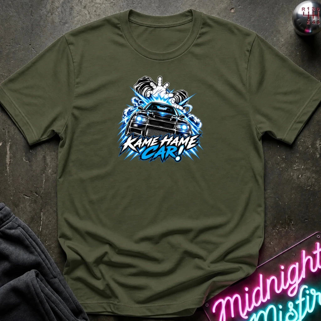 olive green short-sleeve graphic t-shirt laid flat on a dark textured surface. The shirt features a red, white, and black graphic of a car with the text 'KAME HAME CAR!' in stylized lettering.