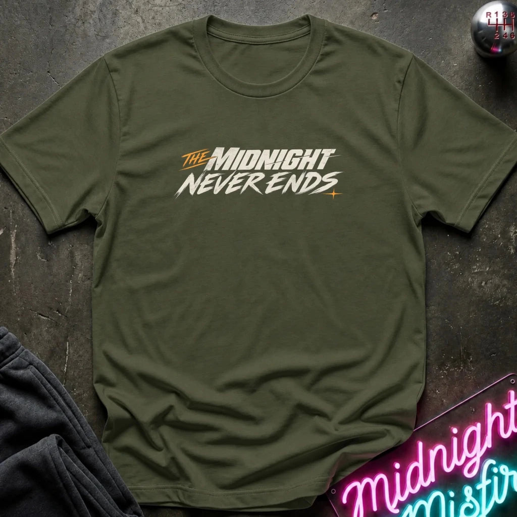 An olive green short-sleeve t-shirt with a graphic print reading 'THE MIDNIGHT NEVER ENDS' in white and orange, laid flat on a dark textured surface with a neon sign and dark pants partially visible.
