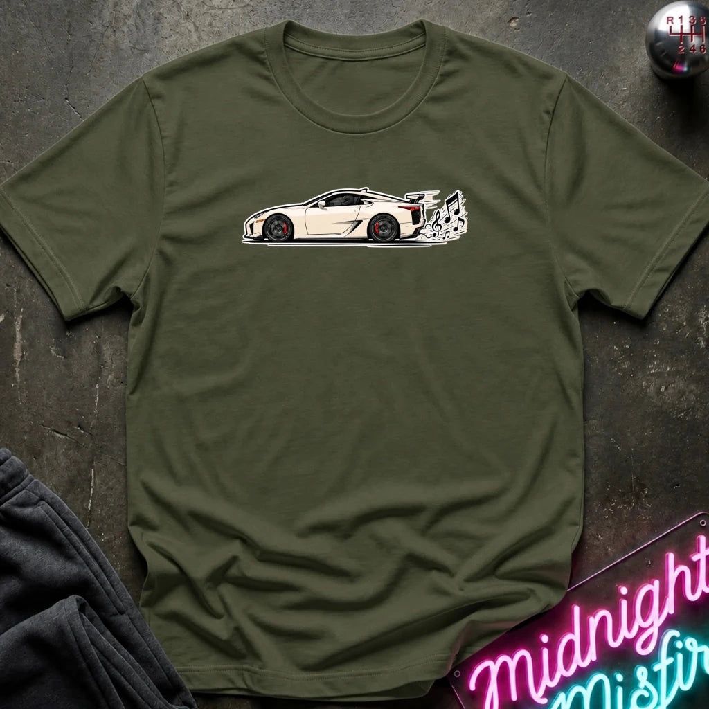 An olive green crewneck t-shirt featuring a white and black side-profile graphic of a sports car on the chest, laid flat on a dark textured surface with a neon sign and dark pants partially visible.