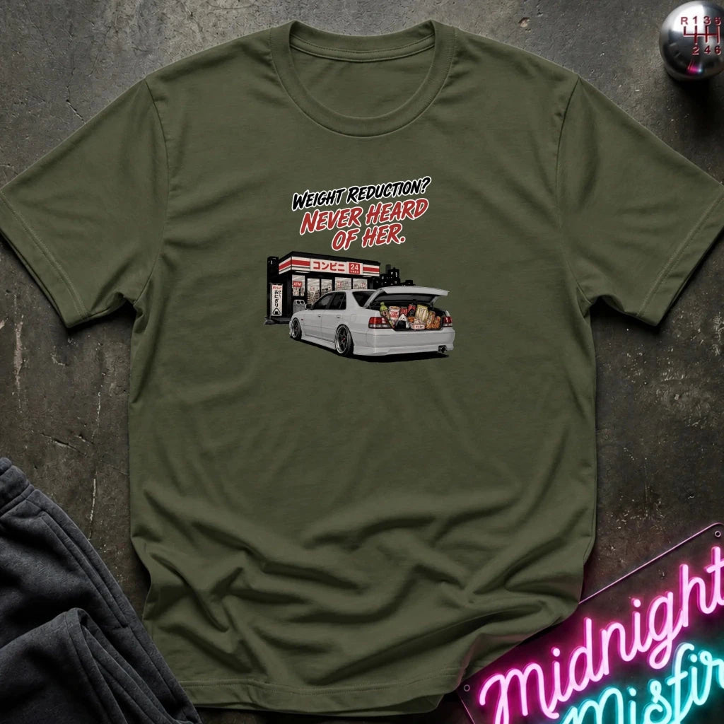 An olive green short-sleeve t-shirt with a graphic print of a white car and the text 'WEIGHT REDUCTION? NEVER HEARD OF HER.' laid flat on a dark textured surface with lifestyle props.