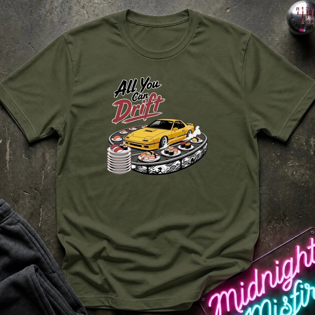 An olive green graphic t-shirt laid flat on a dark textured surface. The graphic features a yellow sports car surrounded by sushi and the text 'All You Can Drift'.