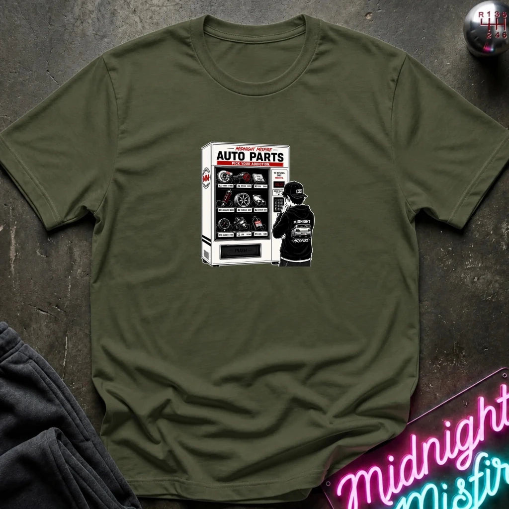 A olive green short sleeved t-shirt featuring a person in front of a vending machine  with car parts.
