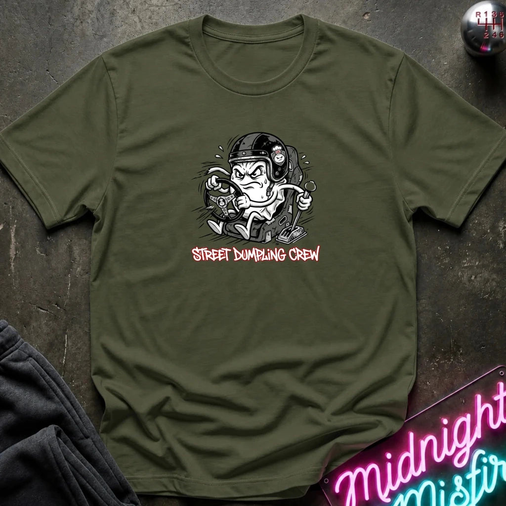An olive green crewneck t-shirt laid flat on a dark textured surface. The shirt features a graphic of a street-dumper character with the text 'STREET DUMPING CREW' in red below.