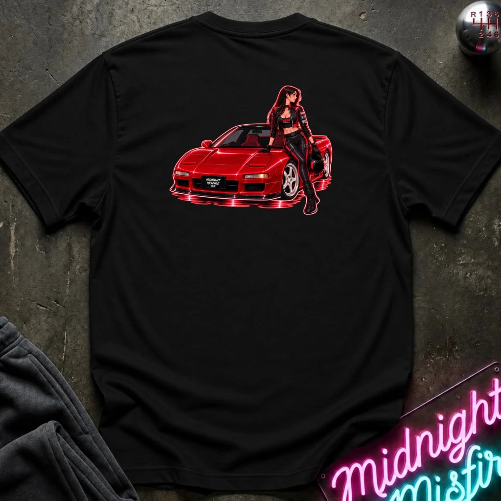 A black short-sleeve t-shirt laid flat on a dark textured surface, featuring a graphic print of a red sports car with a woman leaning on it in pink neon-style outlines. 