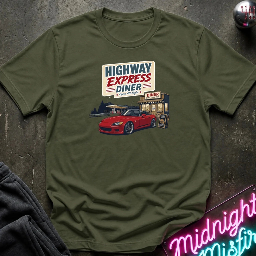 An olive green short-sleeve t-shirt laid flat on a dark textured surface, featuring a retro-style graphic of a red convertible car in front of a diner with the text 'HIGHWAY EXPRESS DINER'.