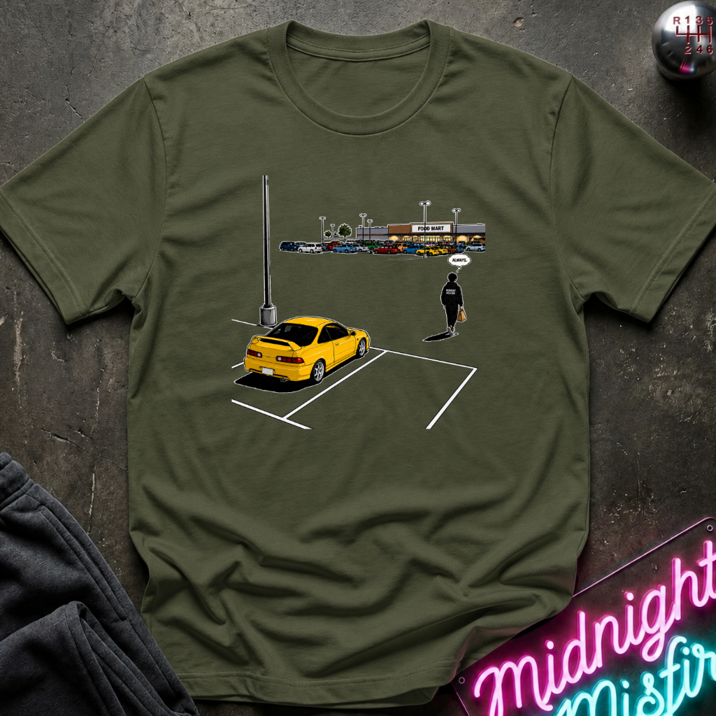 An olive green short-sleeve t-shirt laid flat on a dark textured surface, featuring a graphic print of a yellow sports car parked in a spot with a small figure standing.