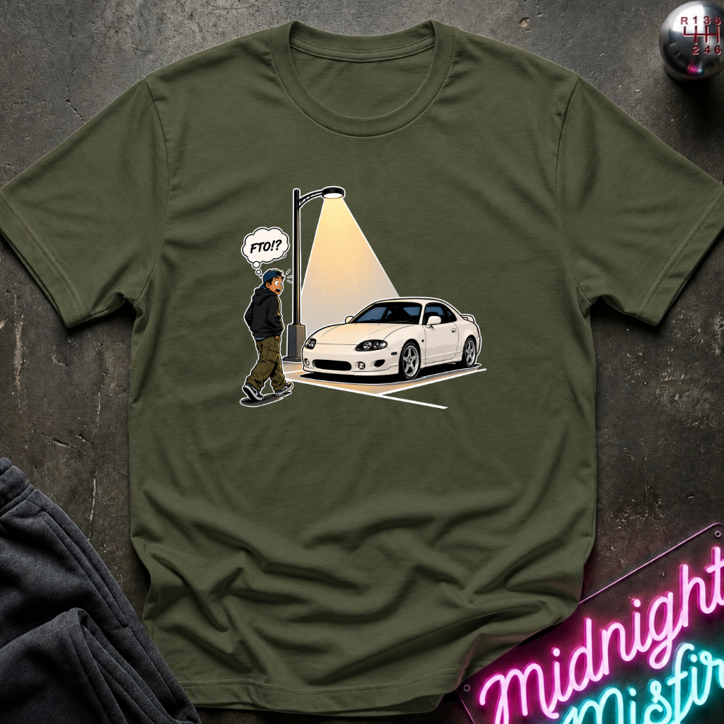 An olive green short-sleeve t-shirt laid flat on a dark textured surface, featuring a graphic print of a white sports car under a streetlamp with a cartoon figure.