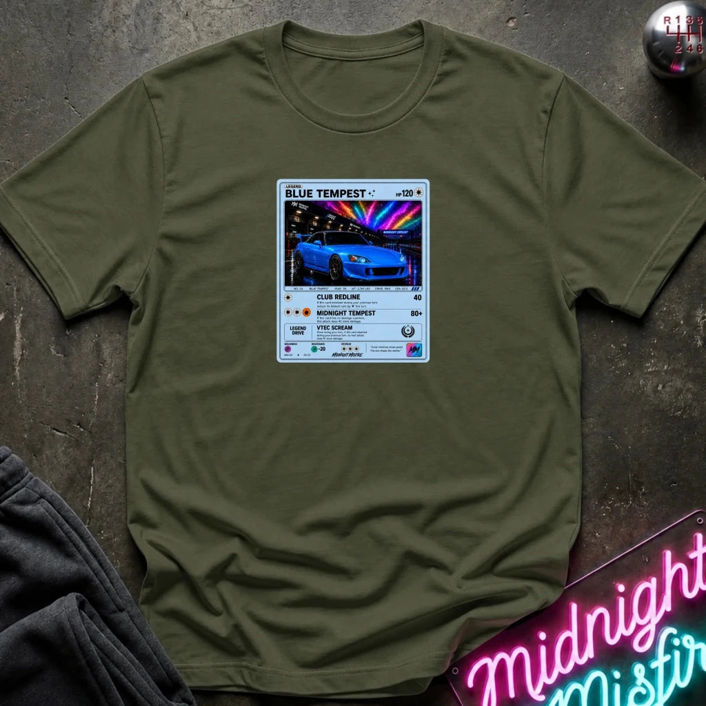 An olive green crewneck t-shirt laid flat on a dark textured surface, featuring a graphic print of vintage card and a car.