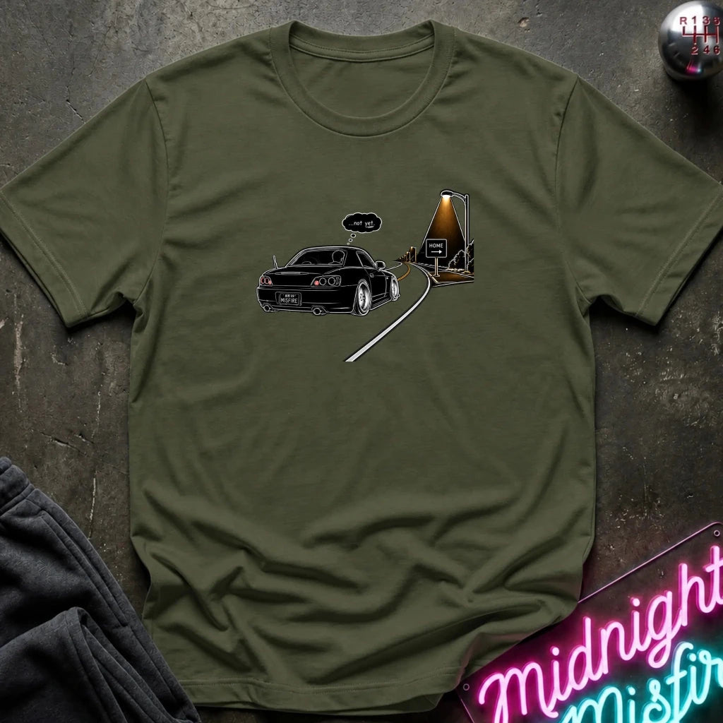 An olive green short-sleeve t-shirt laid flat on a dark textured surface, featuring a graphic print of a black sports car driving passed sign that says home.