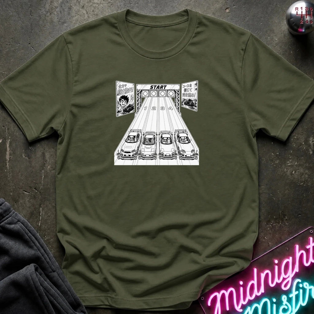 An olive green crewneck t-shirt featuring a white graphic of four cars on a racetrack starting line with a 'START' finish line. The shirt is laid flat on a dark textured surface with a neon sign and dark pants partially visible.