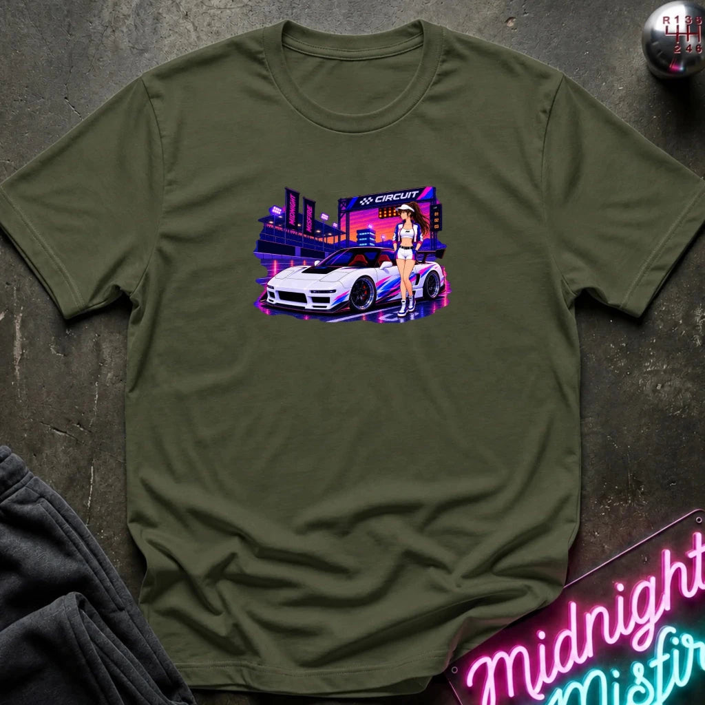 An olive green  short-sleeve t-shirt laid flat on a dark textured surface, featuring a colorful graphic print of a white sports car and a woman in a neon-lit scene. 