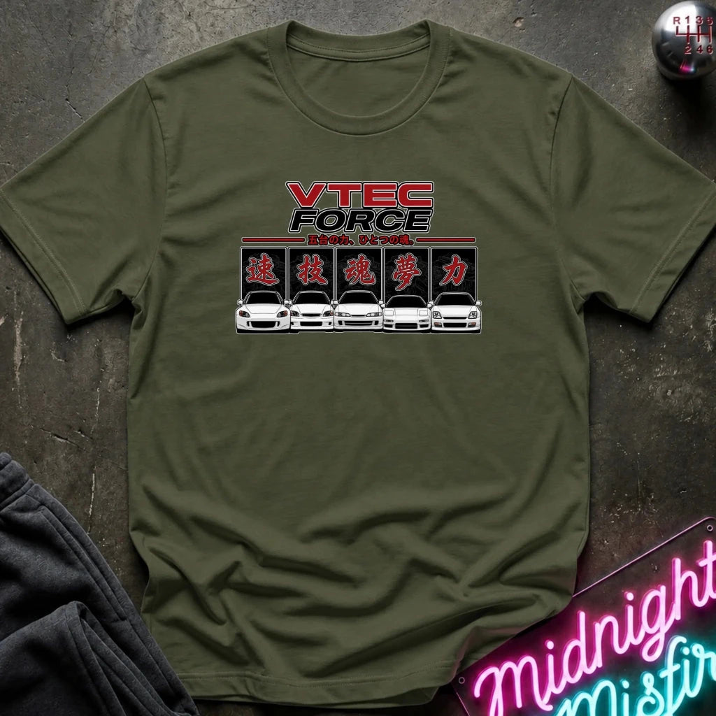 An olive green crewneck t-shirt featuring a 'VTEC FORCE' graphic print on the chest, laid flat on a dark textured surface with a neon sign and dark pants partially visible in the corners.