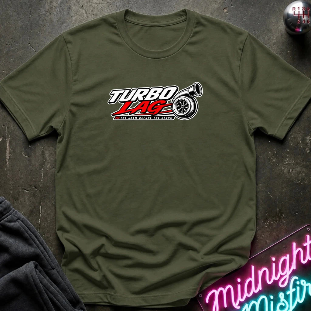 An olive green short-sleeve t-shirt laid flat on a dark textured surface, featuring a 'Turbo Lag' graphic on the chest with a red and white logo and a tire illustration.