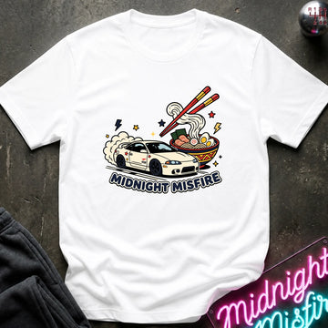 A white short-sleeve graphic t-shirt laid flat on a dark textured surface. The graphic features a white sports car with smoke, chopsticks, ramen noodles, and the text 'MIDNIGHT MISFIRE'.
