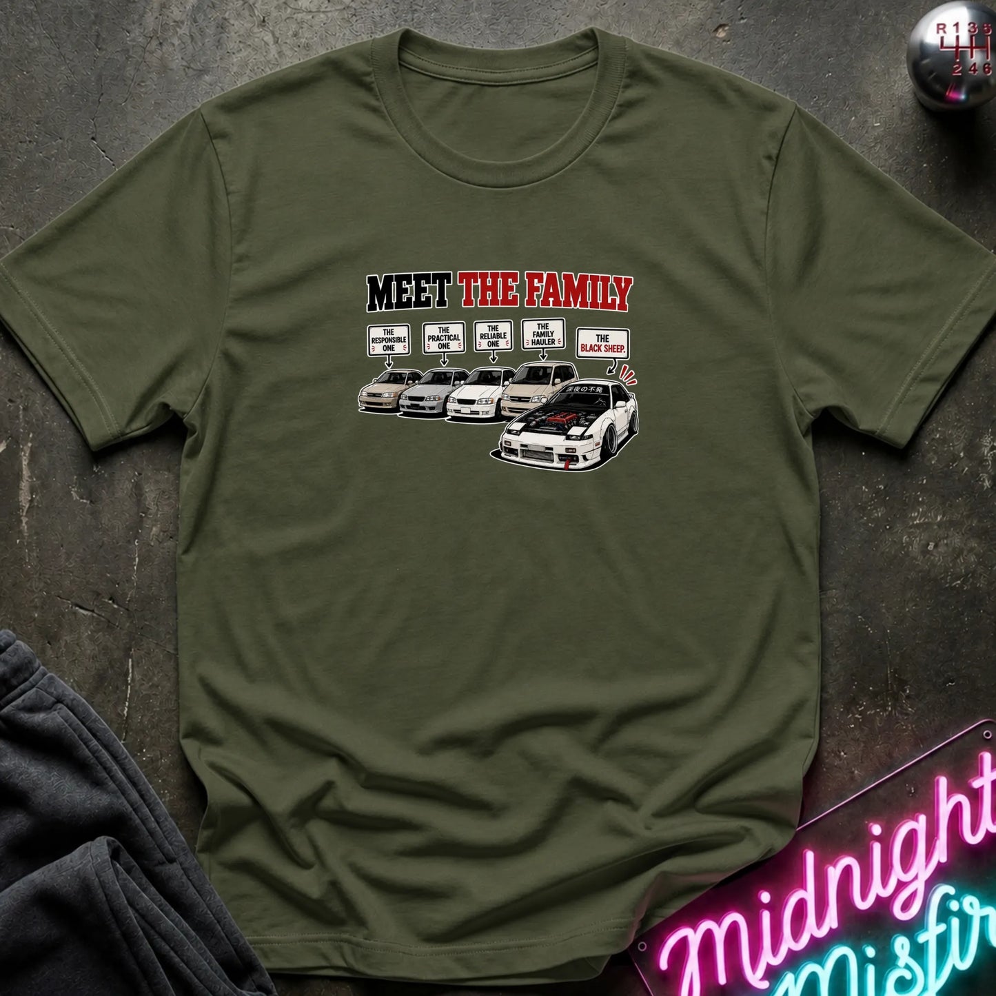 An olive green short-sleeved t-shirt  that has a cars parked with one standing out that says black sheep.