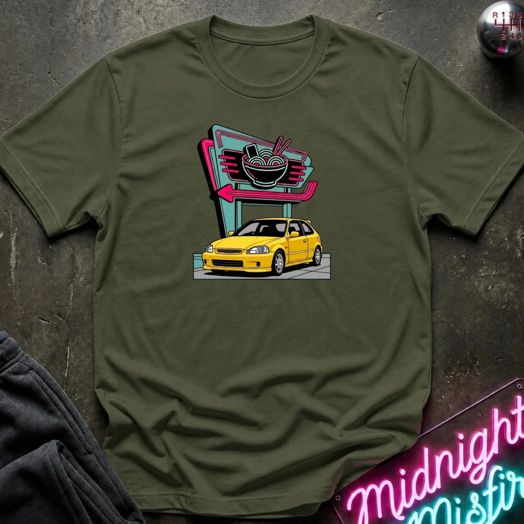 An olive green short-sleeve t-shirt laid flat on a dark textured surface, featuring a retro-style graphic of a yellow hatchback car parked in front of a neon ramen shop sign. 