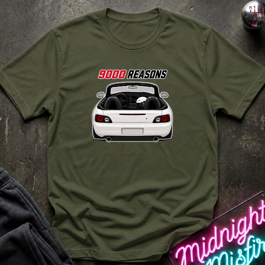 An olive green short-sleeve t-shirt laid flat on a dark textured surface, featuring a graphic of a white convertible car with the text '9000 REASONS' above it. A neon sign and folded dark fabric are partially visible around the edges.