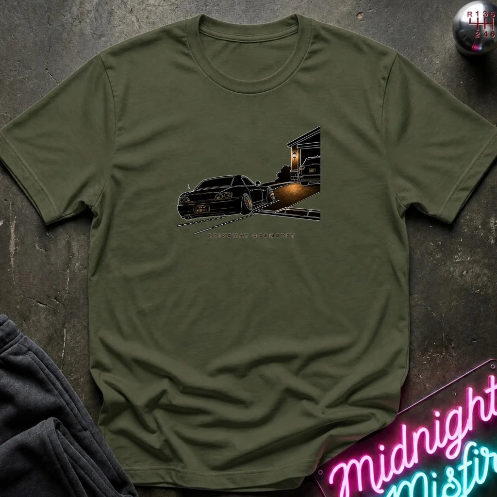An olive green short-sleeve t-shirt laid flat on a dark textured surface, featuring a graphic print of a black classic car going up the driveway.