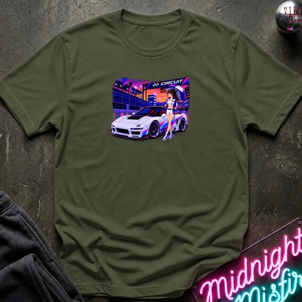 An olive green short-sleeve t-shirt laid flat on a dark textured surface, featuring a colorful graphic print of a white sports car and a woman in a neon-lit scene. 