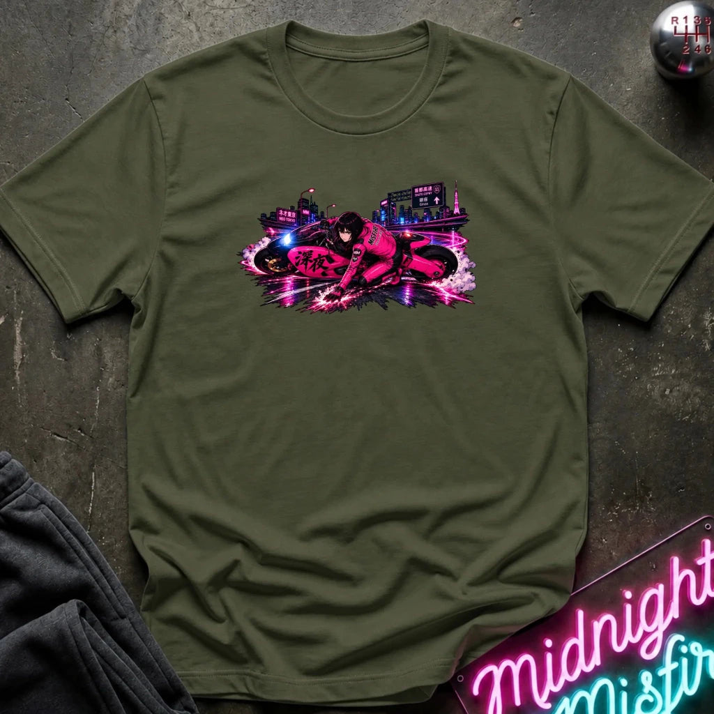 An olive green short-sleeve t-shirt with a vibrant pink and purple neon-style graphic of a motorcycle and city scene on the chest, laid flat on a dark textured surface with a neon sign and dark pants partially visible.